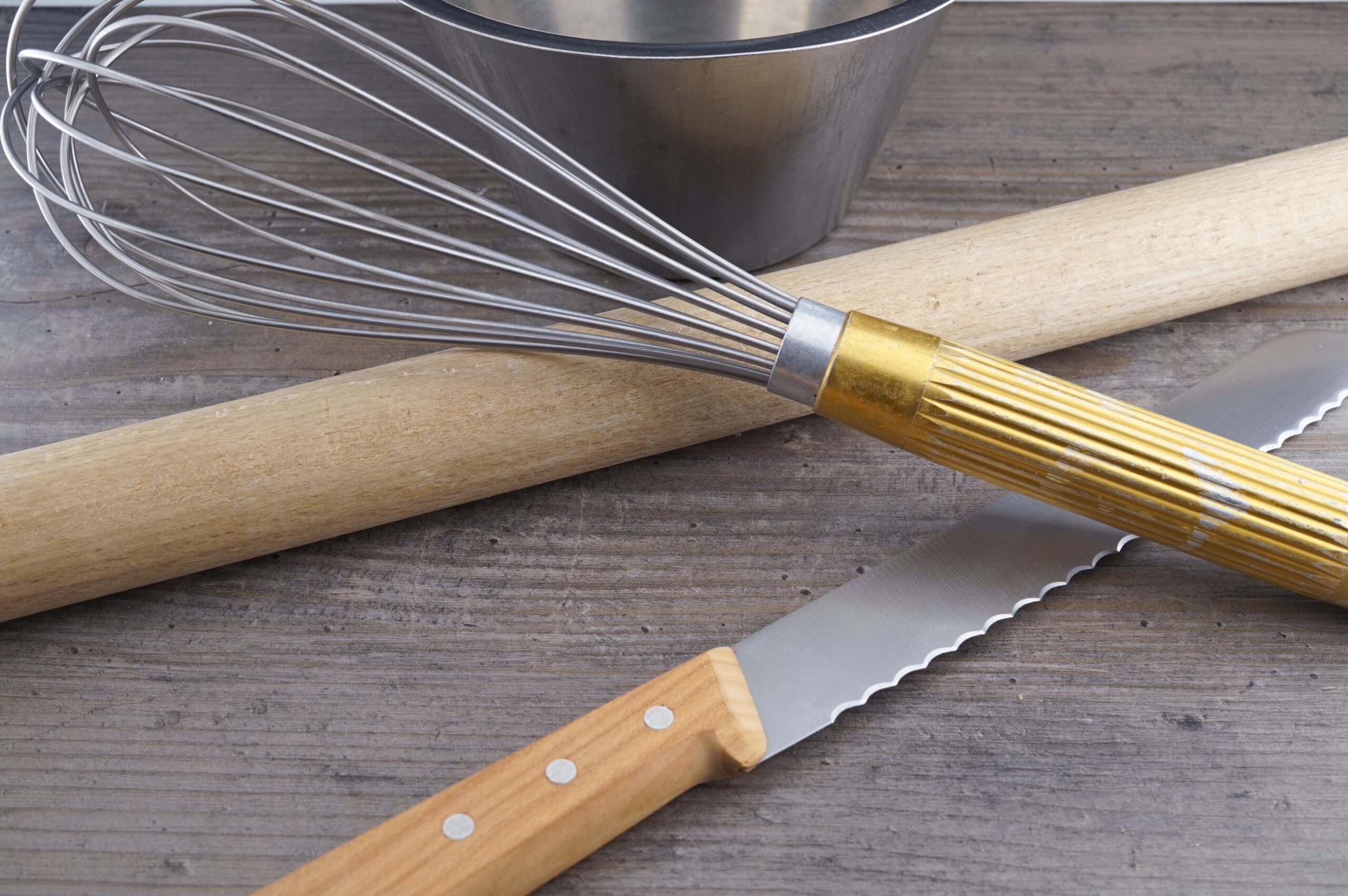 Schwingbesen, Wallholz, Messer und Schüssel auf einer Küchenarbeitsfläche – typische Utensilien für die Teig- und Backvorbereitung.